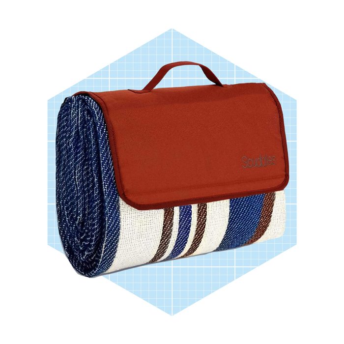 A rolled-up picnic blanket with a brown flap is resting against a light blue, hexagonal background, featuring various linear patterns in blue, brown, and white.