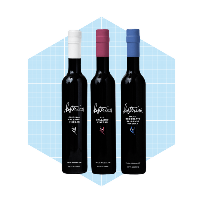 Three bottles of balsamic vinegar are displayed, each with distinct colored caps, set against a light blue geometric background.