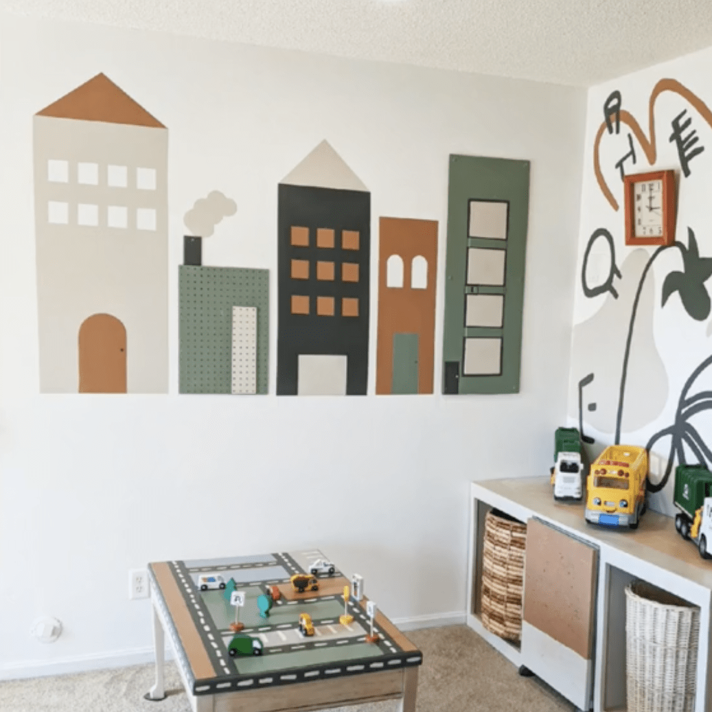 A playroom features painted buildings on the wall, a traffic-themed play table with toy cars, and storage containing vehicles, creating a vibrant, interactive environment.