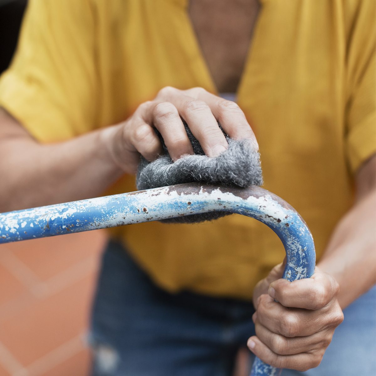 A hand scrubs a rusty blue metal bar with a gray cleaning pad, focused on restoring its surface in a casual indoor setting.