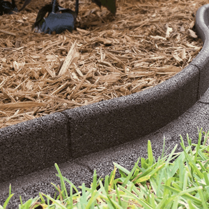 A curved black border outlines a garden bed filled with wood mulch, separating it from a patch of green grass nearby.