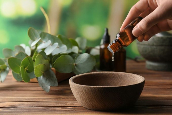 Woman Pouring Eucalyptus Essential Oil Into Bowl On Wooden Table