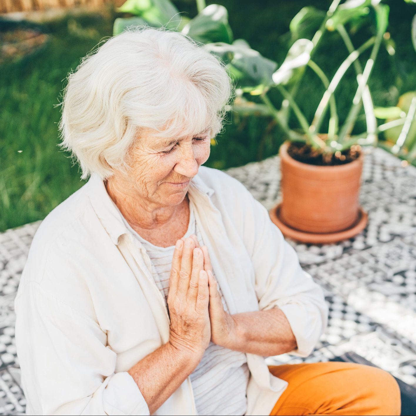 Senior woman doing yoga in the backyard at sunny day.