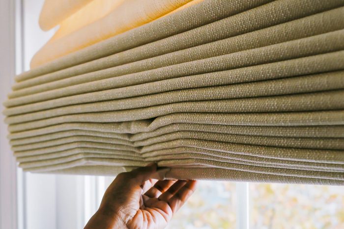 hand pulling down Thermal Curtains to cover window and save energy