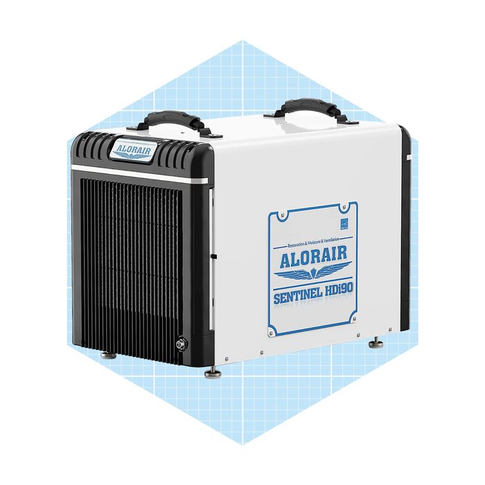 A compact dehumidifier is placed on a light blue grid background, featuring a black front grille, handles, and a label displaying 