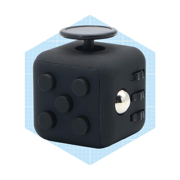A black fidget cube with multiple tactile buttons and a spinning disc sits against a light blue grid background, designed for stress relief and focus.