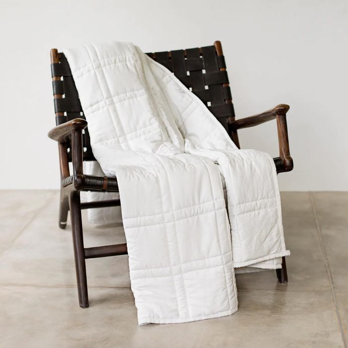 A white quilt drapes over a dark wooden chair, showcasing its texture in a minimalist, light-colored room with a tiled floor.