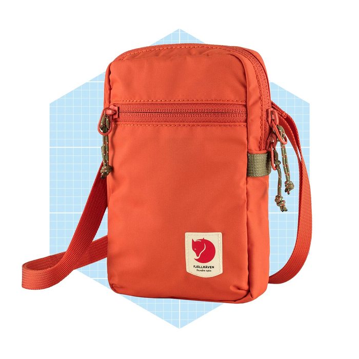 An orange bag with a front zipper and adjustable strap displays a logo. It rests against a light blue hexagonal background with a grid pattern.