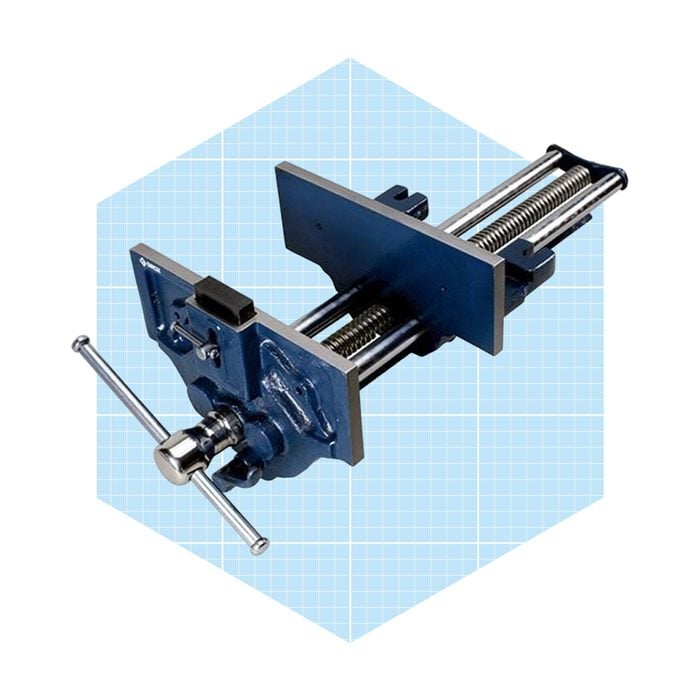A blue metal clamp adjusts a tightened grip, positioned against a light grid background, used for securing objects during machining or assembly tasks.
