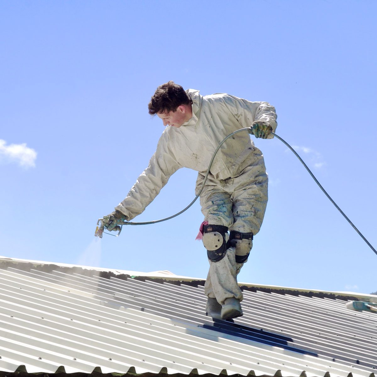 A trademan uses an airless spray to paint the roof of a building