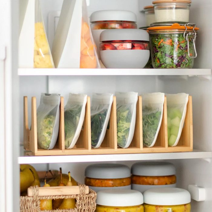 A refrigerator contains organized food items, including jars of salad and fruits, and bags of vegetables in a wooden holder, promoting efficient storage.