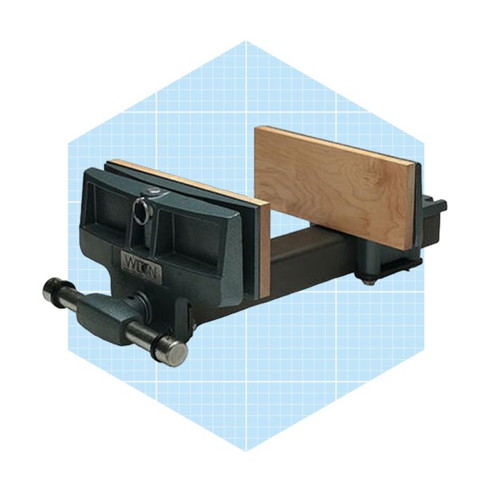 A bench vise holds wooden boards tightly as it is positioned for woodworking tasks, set against a light blue grid background.