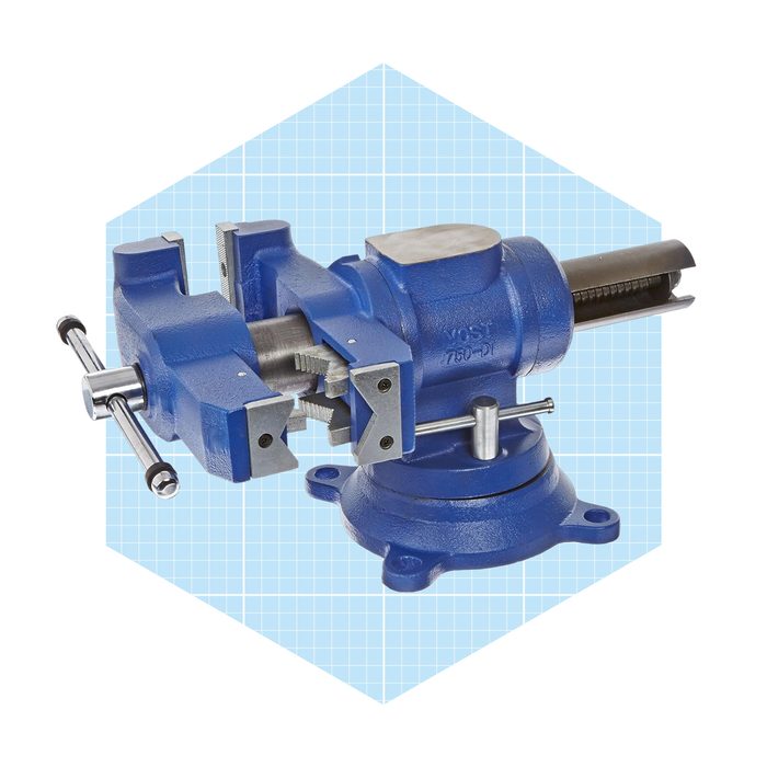 A blue vise is positioned diagonally, clamping a cylindrical object, set against a light blue grid background, suggesting a workshop or tool context.