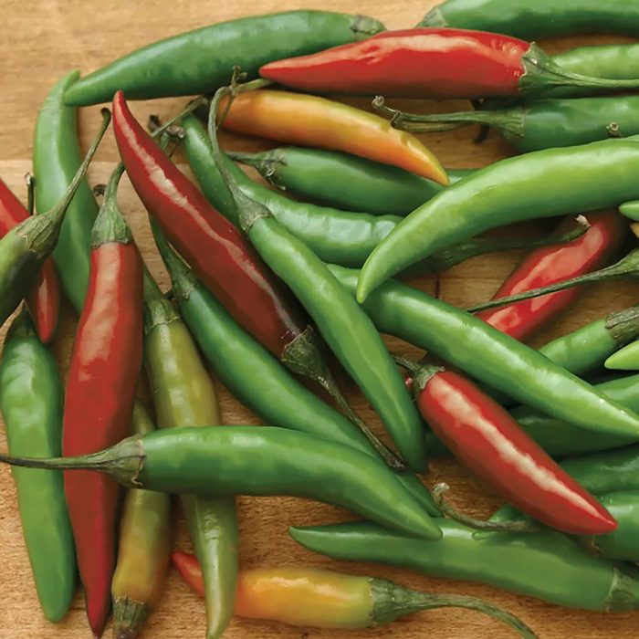 A collection of assorted chili peppers, including green, red, and yellow varieties, is spread across a wooden surface, displaying their vibrant colors and shapes.