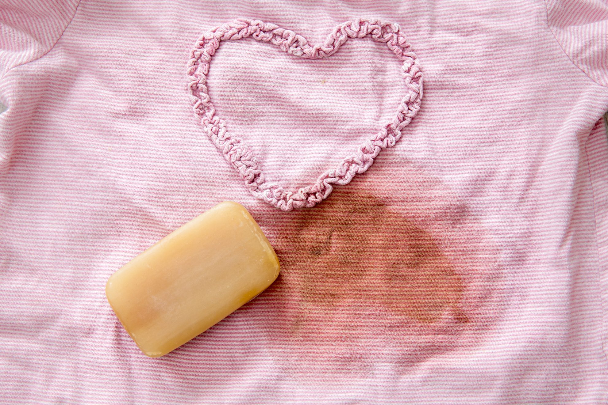 Removing stains with bile( gall, sap) soap bar. Natural chemical free household clothing washing products concept. Flat lay view of brown soap bar on pink blouse next to big stain.
