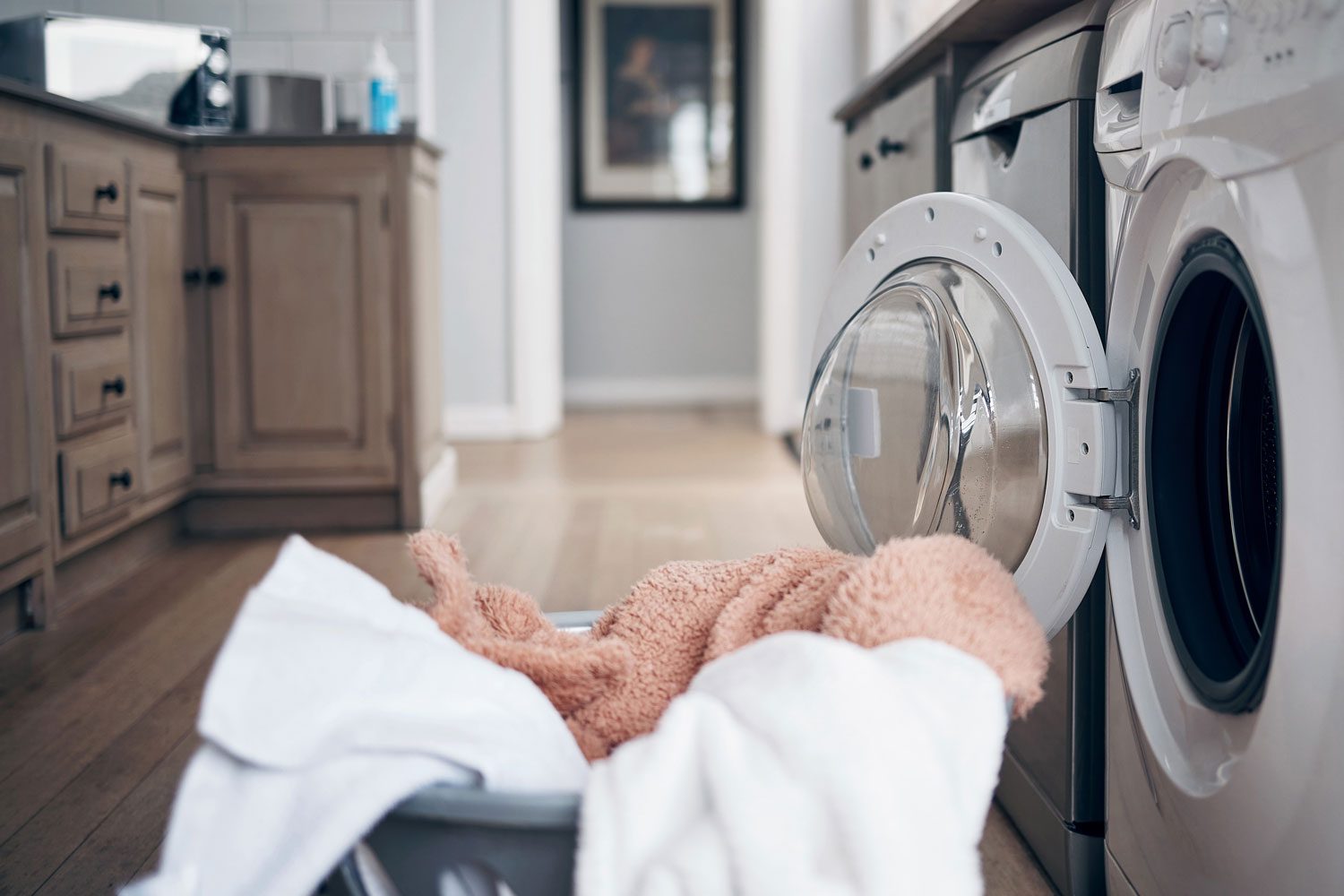 Shot Of A Laundry Basket Filled With Freshly Dried Clothes Against a Laundry Room Background with the dryer door still open