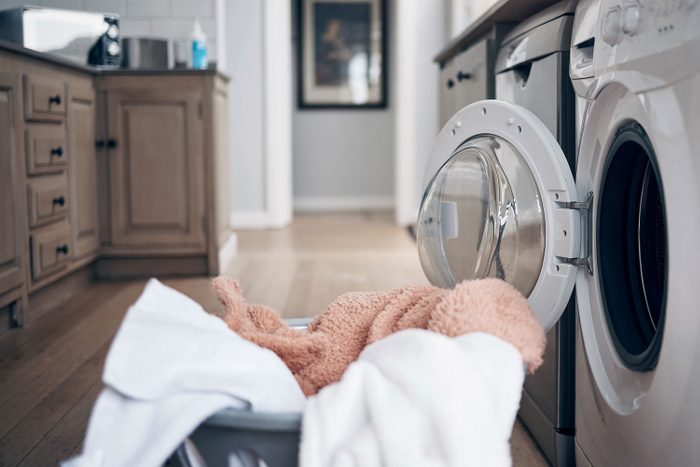 Shot Of A Laundry Basket Filled With Freshly Dried Clothes Against a Laundry Room Background with the dryer door still open