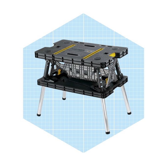 A folding workbench stands upright, supporting tools, with sturdy legs and a textured surface, set against a light blue grid background.