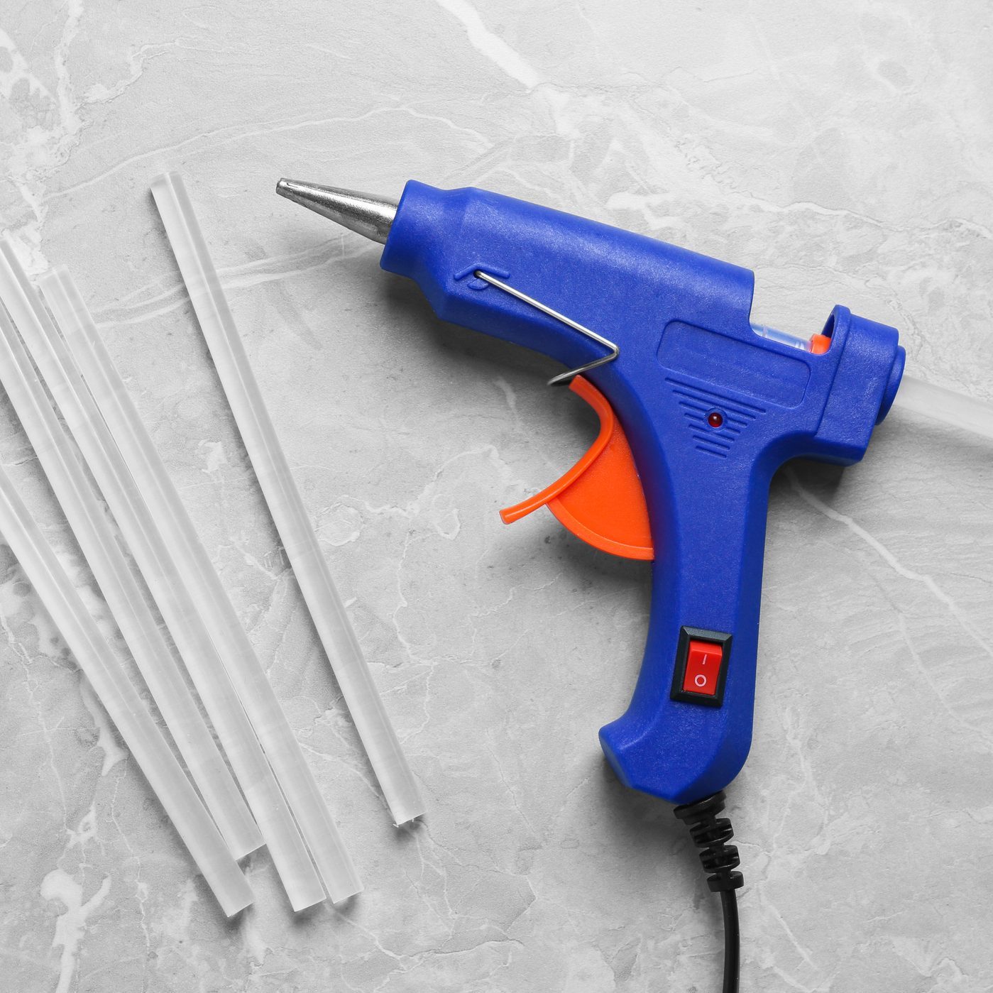 Blue glue gun and sticks on light grey marble table, flat lay