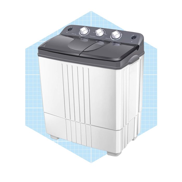 A compact washing machine with a dark top and control knobs, positioned against a light blue geometric background, indicates a modern laundry appliance.