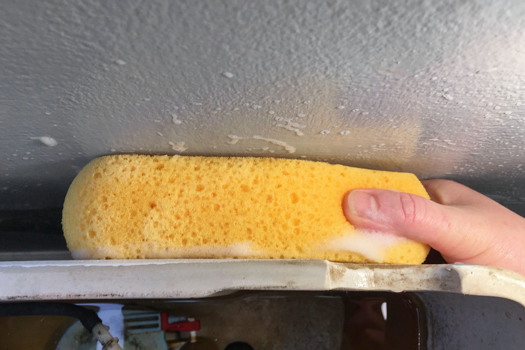 Scrubbing behind toilet with sponge