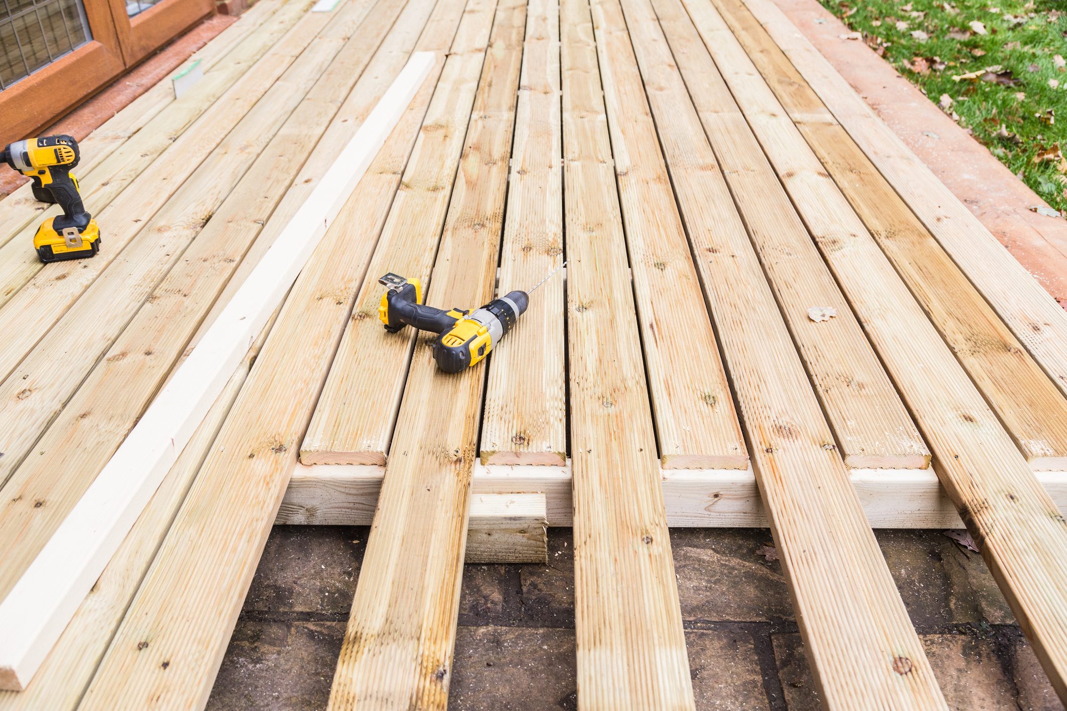 A new wooden, timber deck being constructed. it is partially completed. two drill can be seen on the decking.