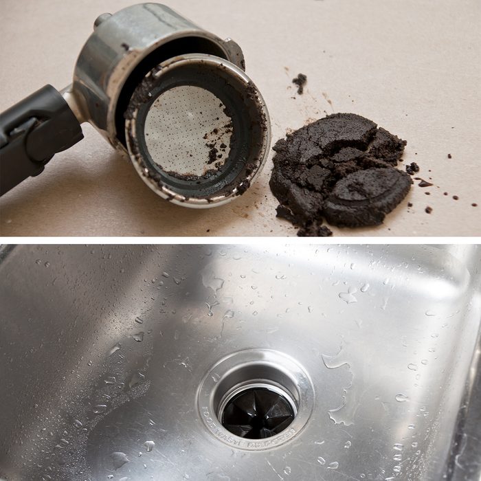 A used coffee portafilter with spent coffee grounds forming a clump next to it. A clean stainless steel kitchen sink with a garbage disposal visible in the drain.