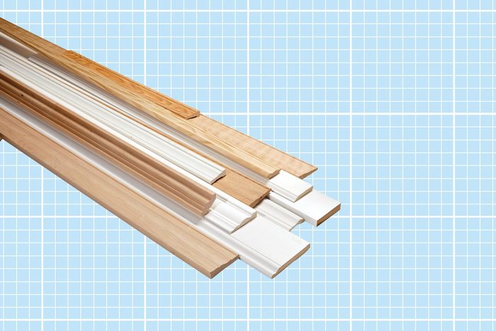 A collection of various types of wooden trim pieces, some painted white and others in natural wood color, displayed on a blueprint-style background. The trims are arranged at different angles, showcasing their profiles and designs.