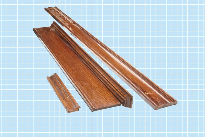 Several pieces of brown wooden molding or trim rest on a light blue grid background. The molding pieces vary in length and design, with one piece significantly shorter than the others. The wood has a polished finish.
