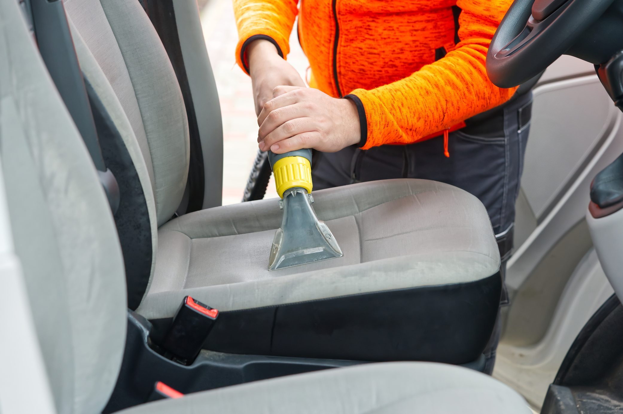 Handyman vacuuming car front textile seat with vacuum cleaner