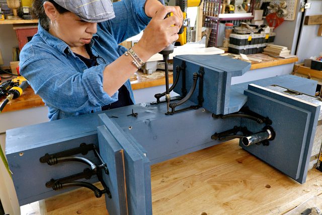 A person in a workshop attaching components to the tower for hose holder.
