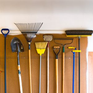 Household and garden tools stored in garage on pegboard wall in an organized and tidy fashion.