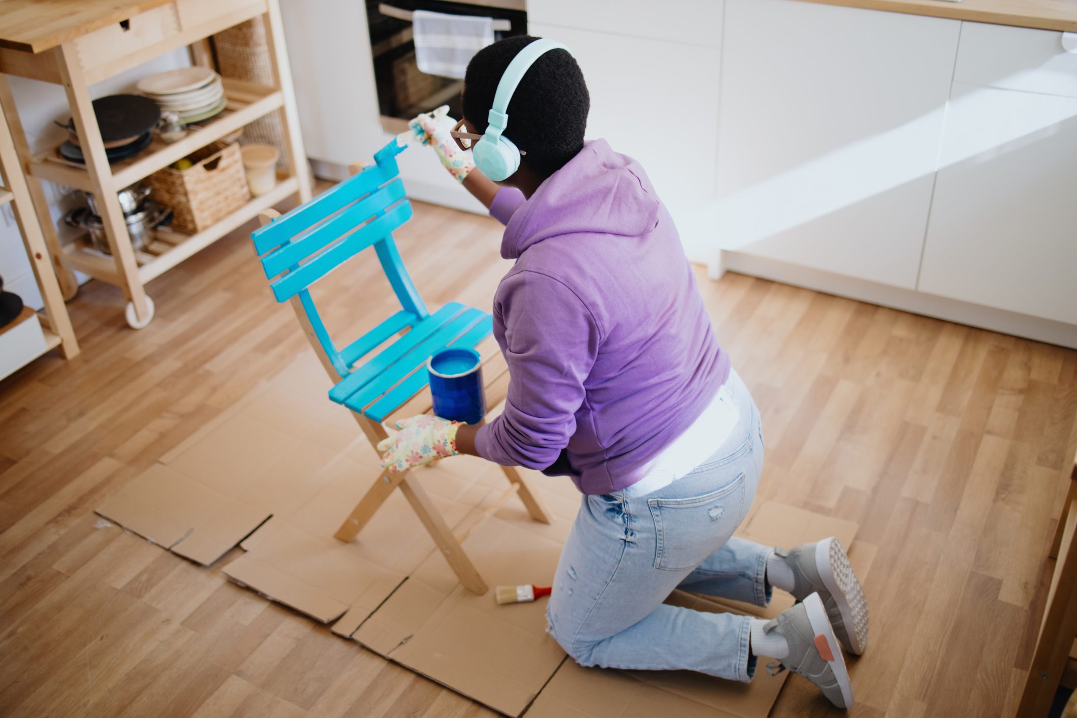 Young woman is painting a chair at home and listening music on wireless headphones