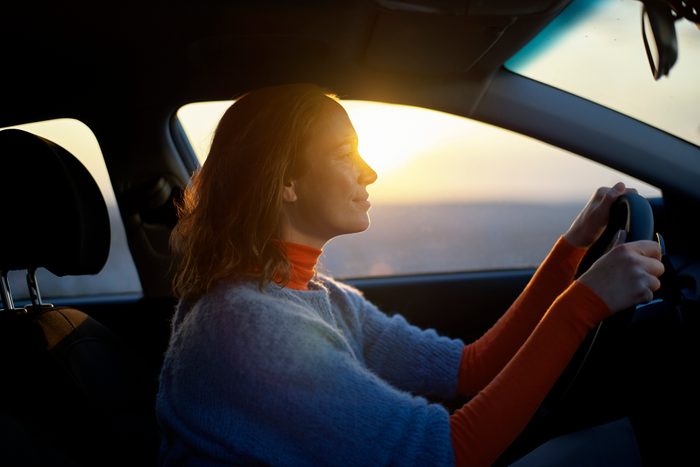 Woman driving a car during sunset with warm light on her face