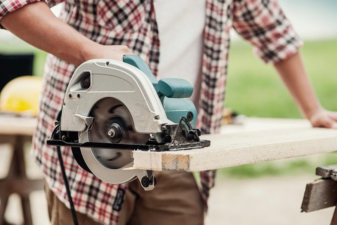 a man cutting wood plank with circular saw.