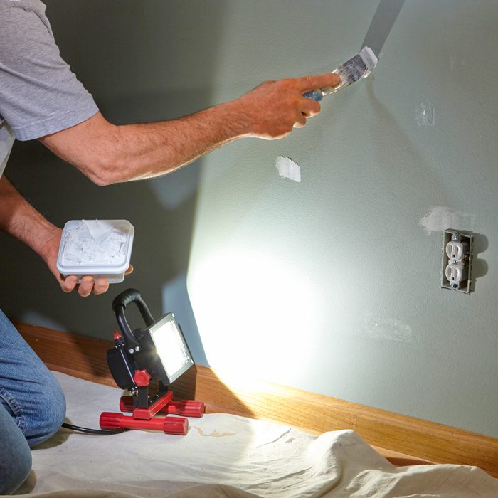 person using raking light while patching wall