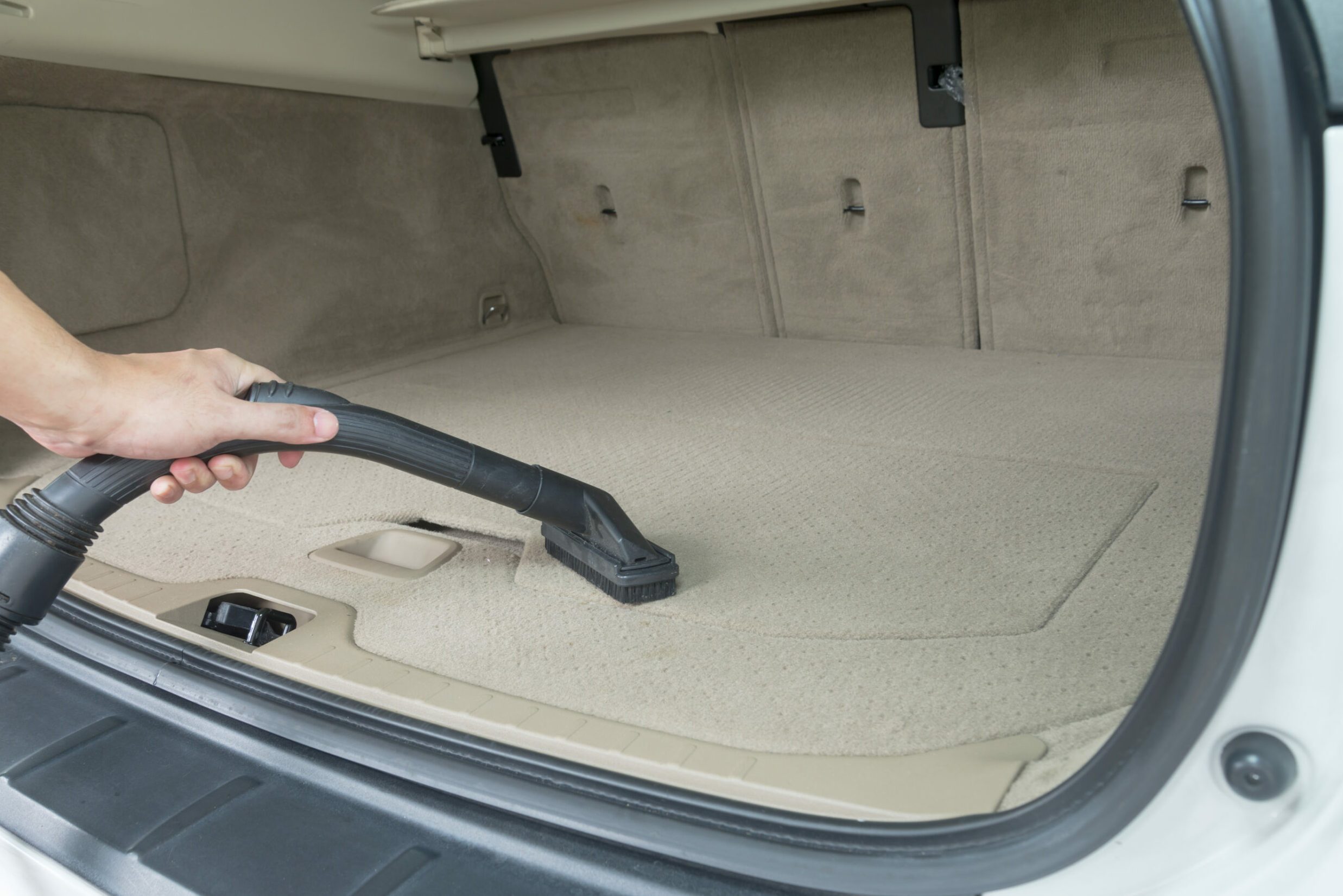 Car interior detailing vacuuming dust from a car carpet in the boot trunk