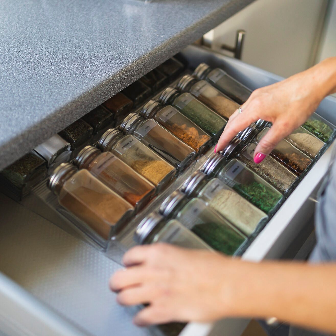 Hands of woman arranging spice jars in kitchen drawer