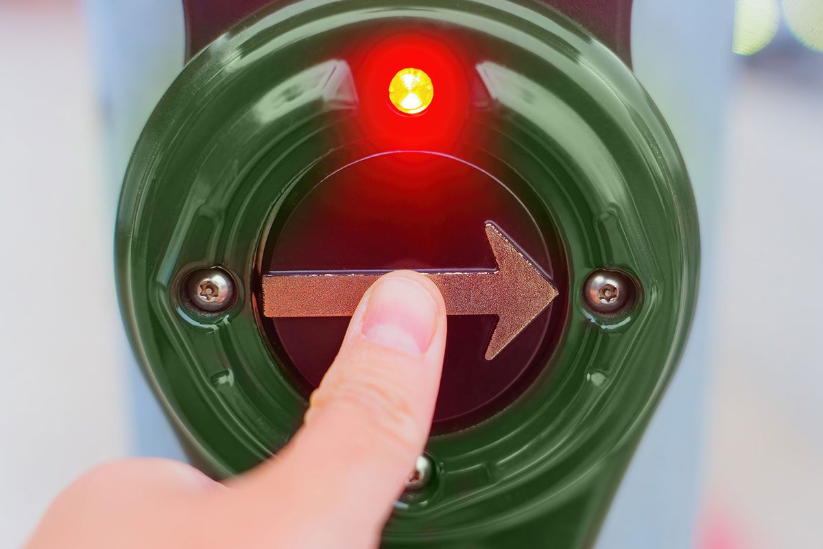 Close-up view of a thumb pressing a pedestrian crossing button,