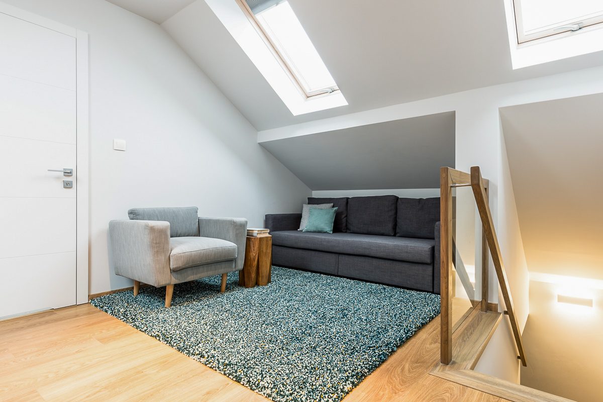Comfortable gray armchair and black sofa in a relax corner of a white attic house interior with roof windows