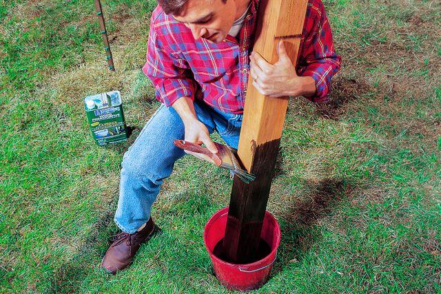 A person applying a black coating to a cedar fence post