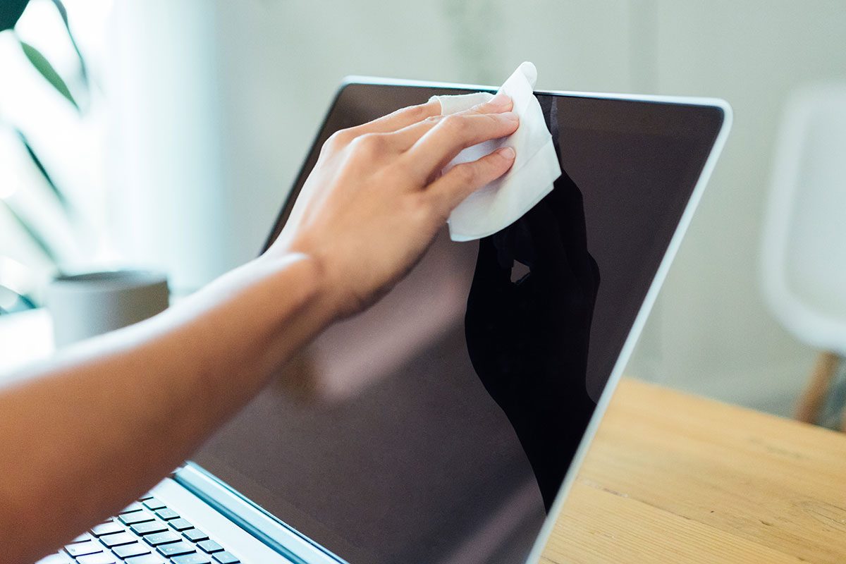 woman cleaning the laptop surface with cleaning wipe