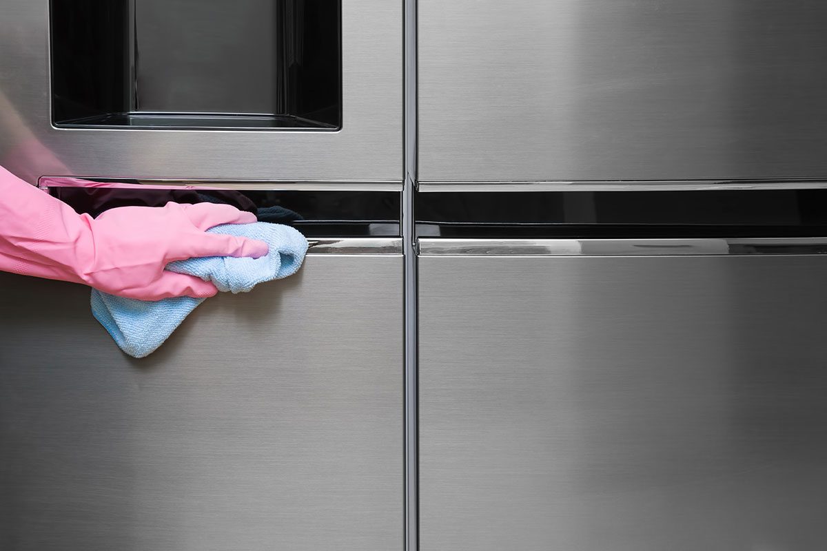 Employee hand in rubber protective glove with micro fiber cloth wiping a fridge's stainless doors.