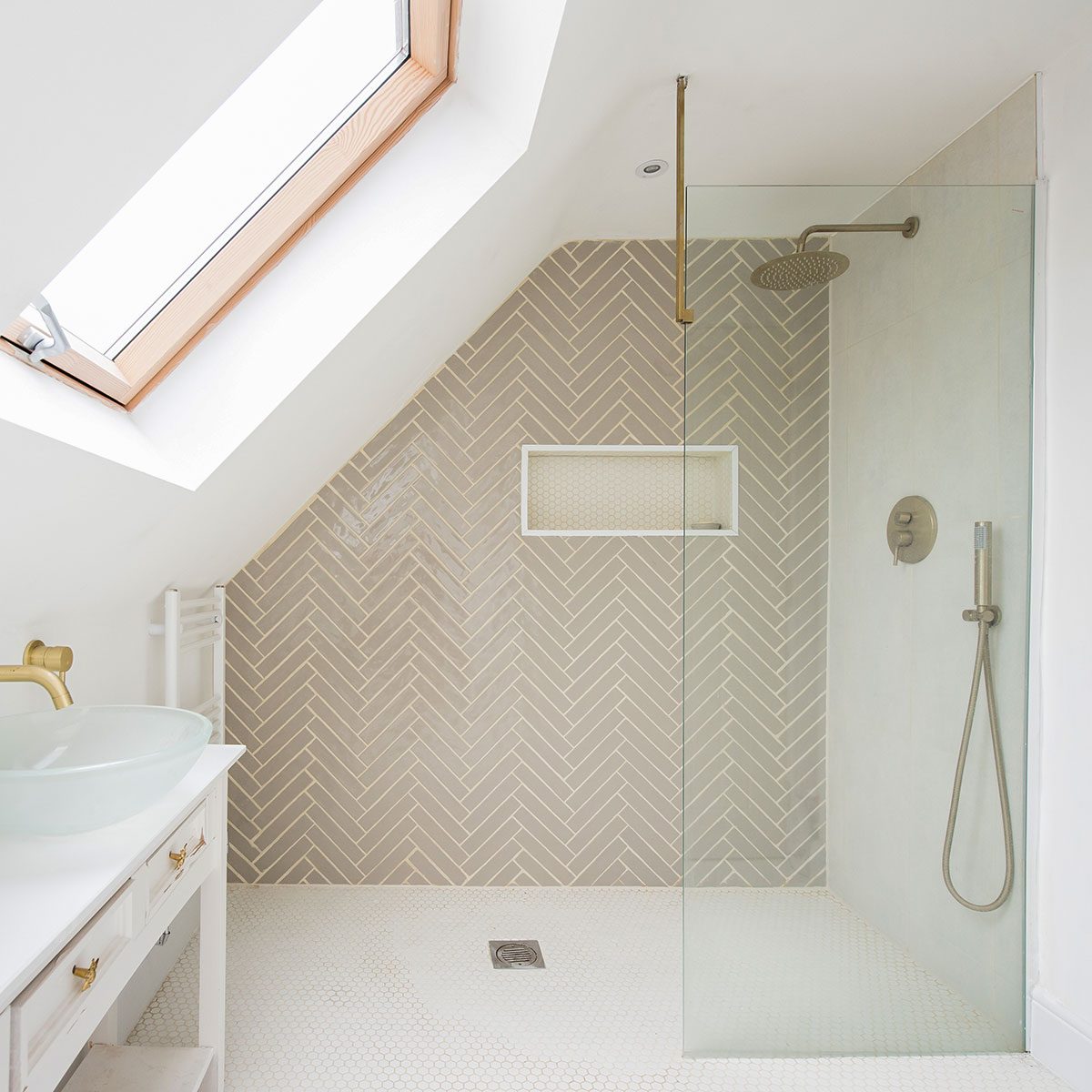 A general interior view of a white bathroom, glass bowl sink on a shabby chic dresser, towel radiator, brushed gold effect tap, skylight, hexagon tiled floor
