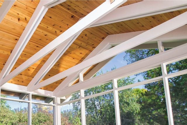 A wooden ceiling with white structural beams extends overhead, while large windows allow natural light and views of greenery outside.
