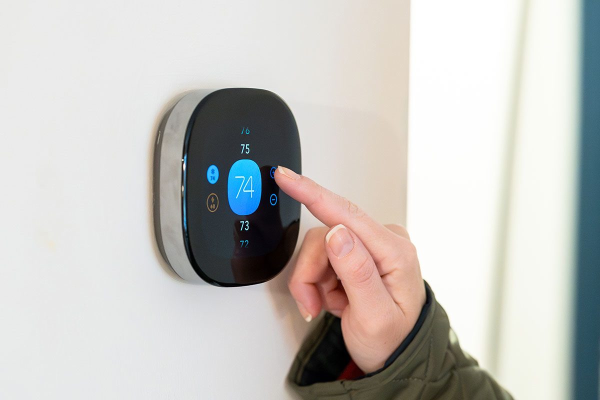 Woman adjusting temperature on digital thermostat