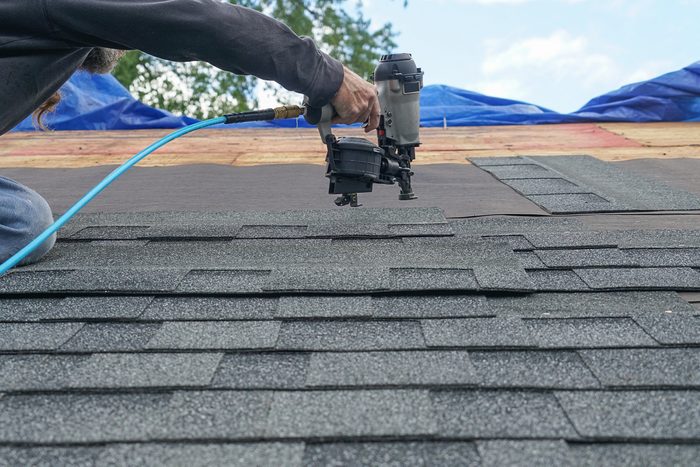 handyman using nail gun to repair roof shingles