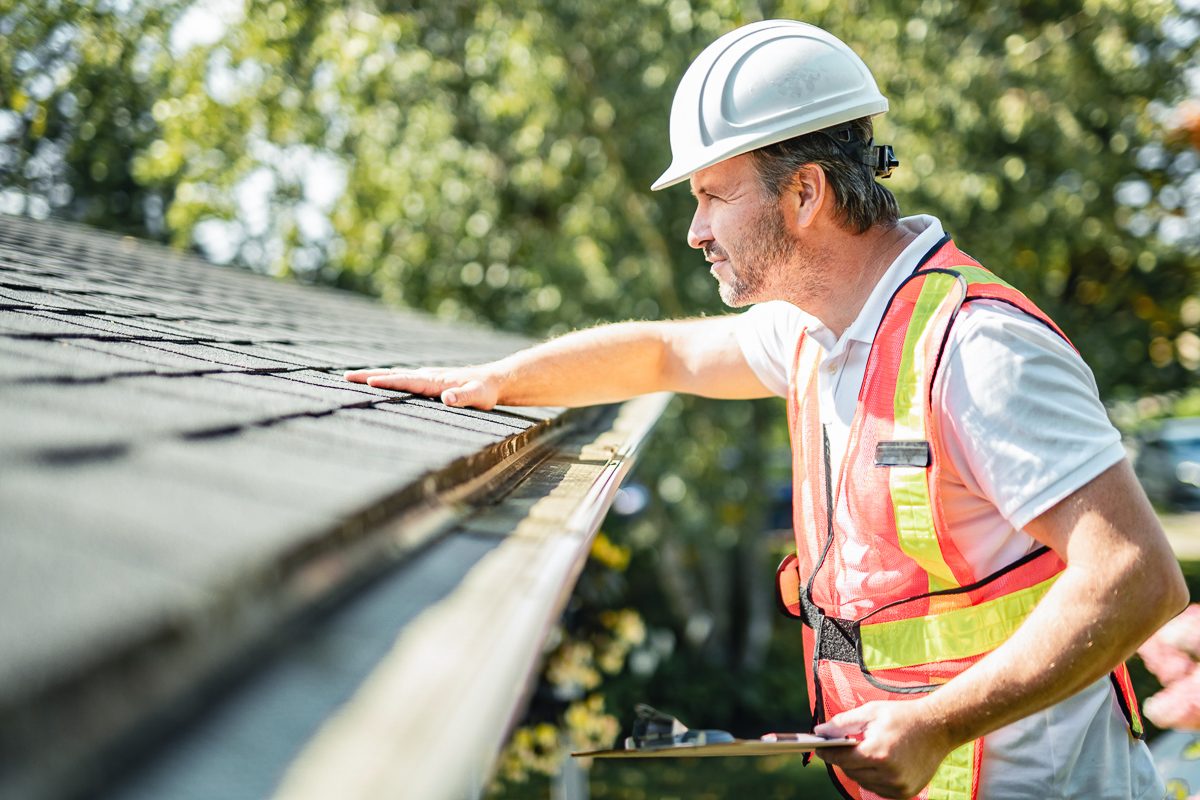 man with clipboard wearing hard hat inspecting house roof