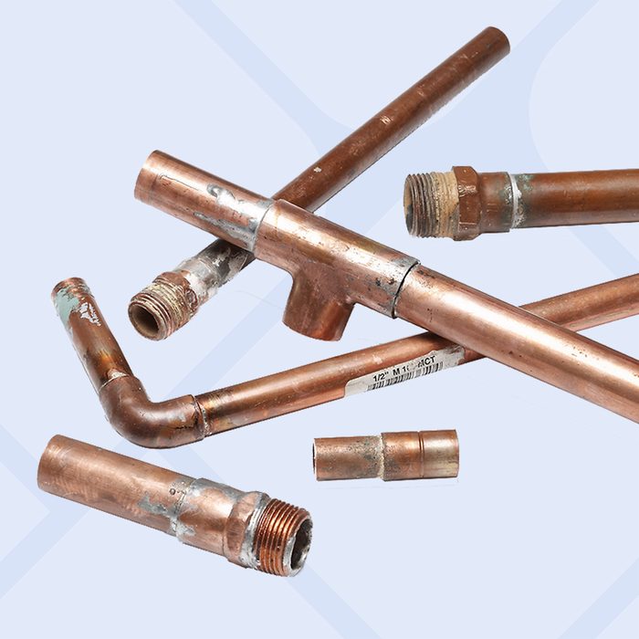 Several copper pipes with threaded and soldered ends, some bent at angles, are arranged on a light surface. The pipes show signs of use and oxidation.