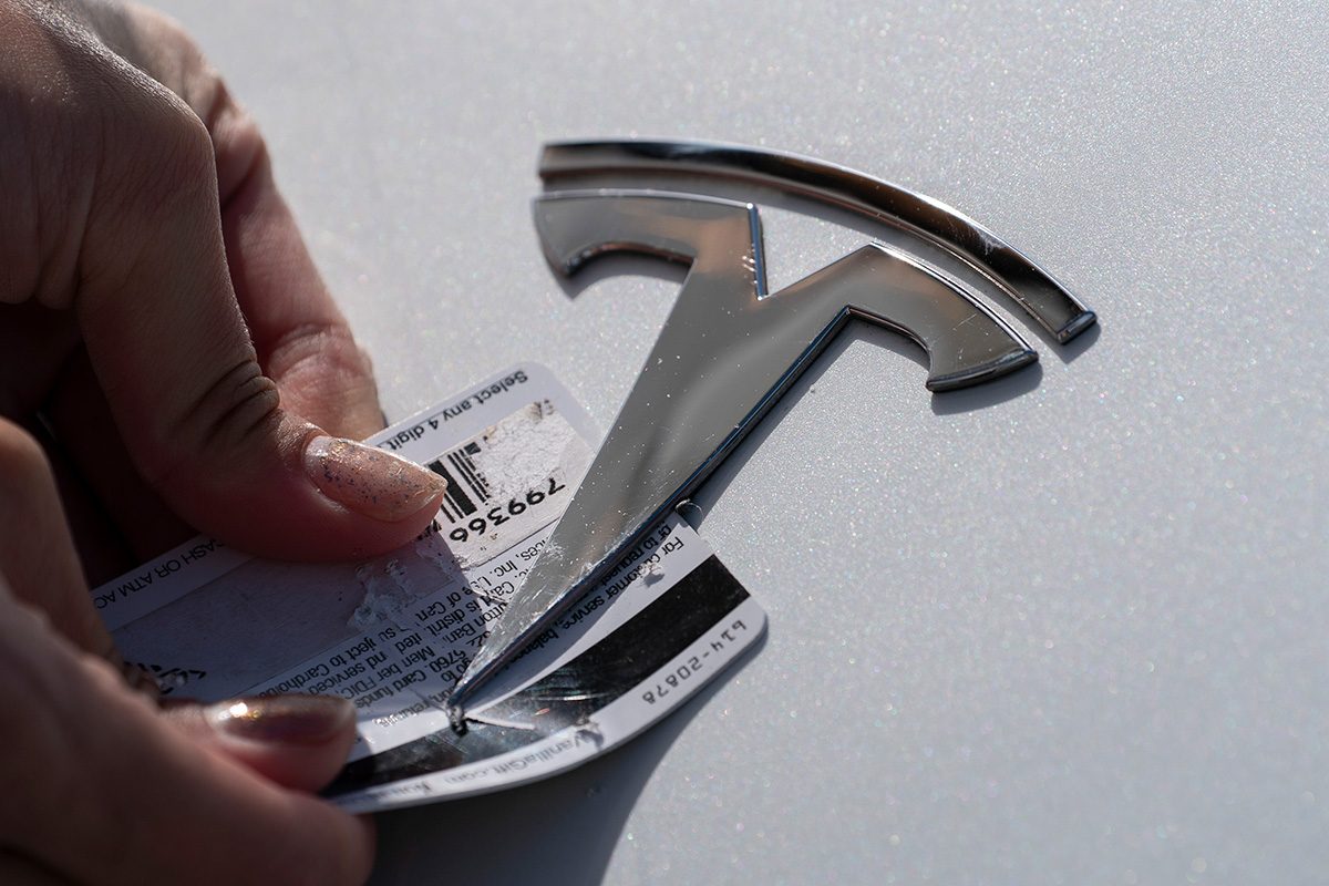 A Tesla emblem is being removed from a Tesla vehicle